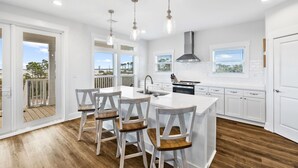 Une cuisine moderne dotée d’un îlot central, de tabourets de bar, de luminaires suspendus et offrant une vue sur l’extérieur.