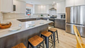 Een moderne keuken met een groot eiland, roestvrijstalen apparatuur en houten barstoelen.