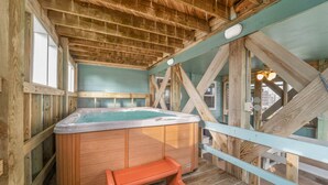 Een houten jacuzzi met een bankje, omgeven door houten balken en een lichtblauwe muur.