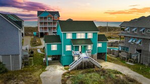 Een woongebied aan de kust met een opvallend turquoise huis, voorzien van een veranda en een trap naar de ingang.