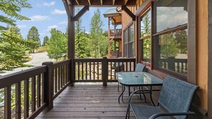 A wooden deck with a table and chairs, overlooking a forested area.