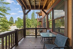 A wooden deck with a table and chairs, overlooking a forested area.