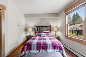 A bedroom with a bed, two bedside lamps, a window with a view of trees and rocks, and a headboard. - Charming Mountain Retreat in Keystone, Colorado (Keystone)
