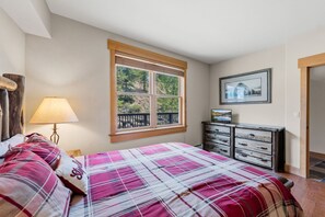 A bedroom with a bed, a nightstand, a dresser, a window with a view of trees, and a framed picture on the wall. - Charming Mountain Retreat in Keystone, Colorado (Keystone)