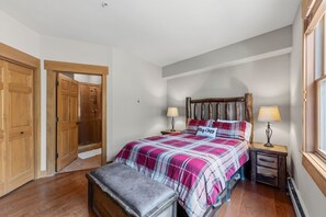 A bedroom with a bed, two bedside tables, a bench, a wooden headboard, and a window.