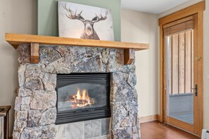 A stone fireplace with a fire, a wooden mantel, and a deer painting above it. - Charming Mountain Retreat in Keystone, Colorado (Keystone)