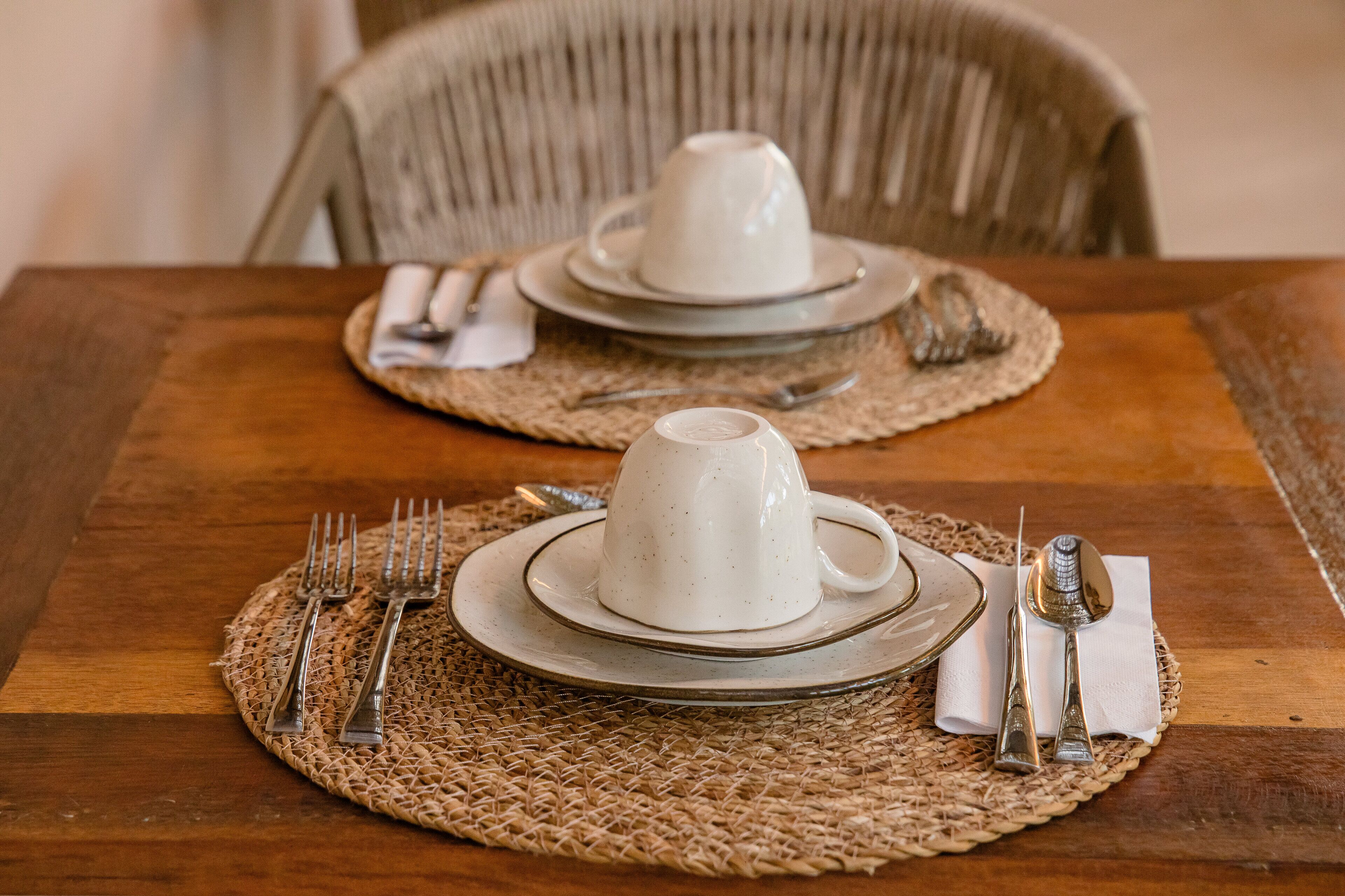A dining table set with white ceramic plates, a white cup, and silverware on a woven placemat.