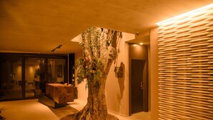 A modern interior with a central tree sculpture, a reception desk, and a wall with horizontal slats. - Pousada Yamandu (São Sebastião)