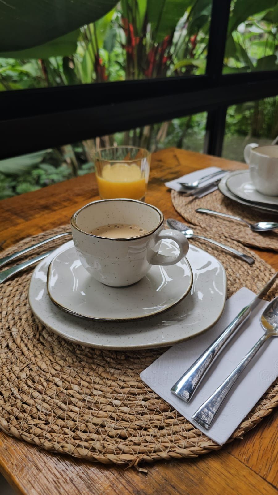 A table with a cup of coffee, a glass of orange juice, and cutlery on a woven placemat.