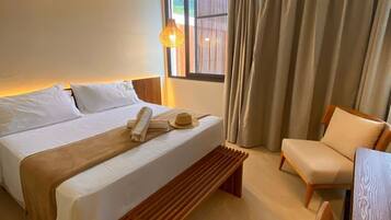 Habitación de hotel con cama, un banco de madera, una silla, un escritorio, un ventilador de techo y una ventana con cortinas.