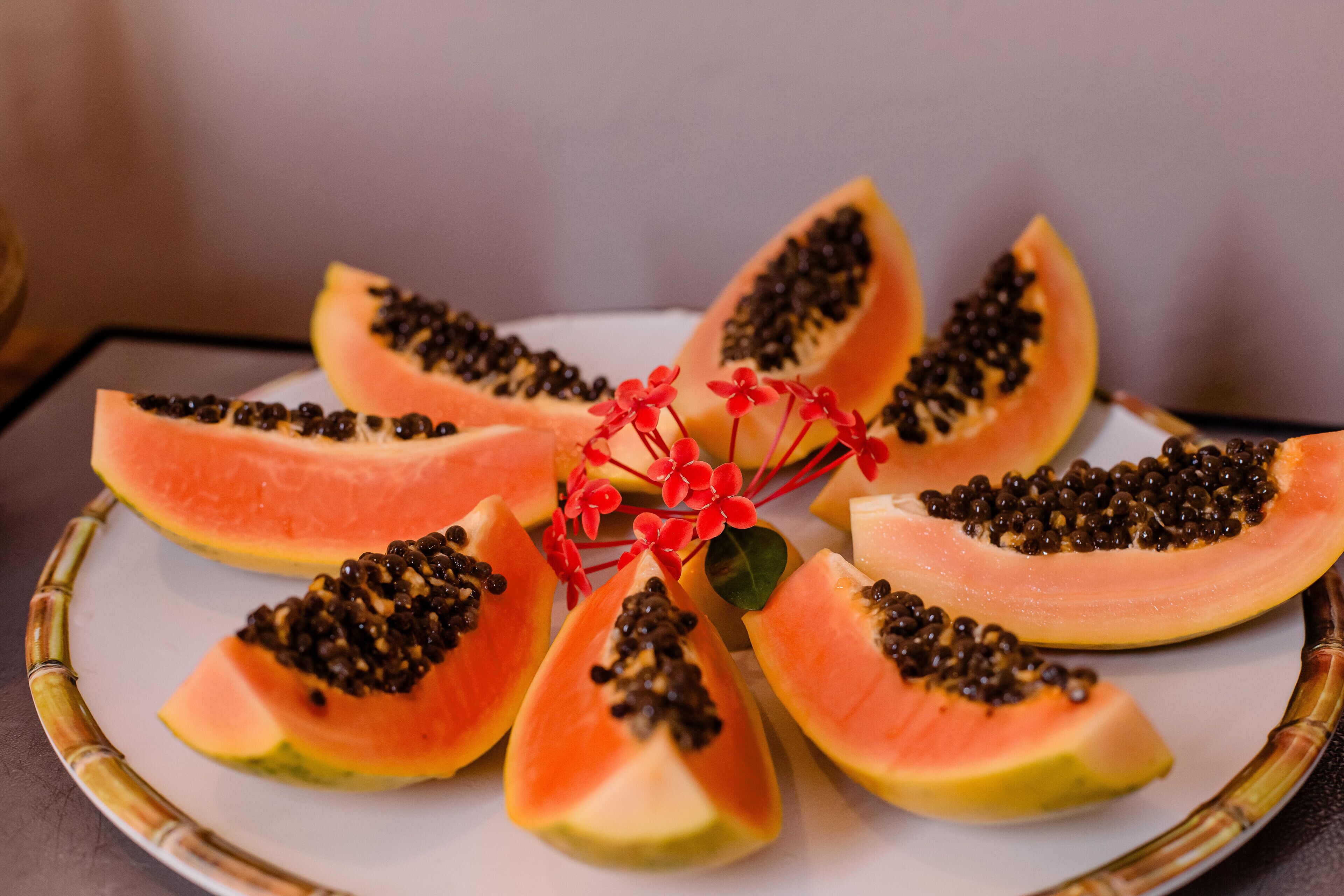 Un plato de papaya en rodajas dispuesta en forma de flor, con una flor roja decorativa en el centro.