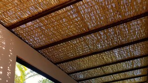 A spacious indoor area with a high ceiling covered in woven material, large windows offering views of greenery, and several wicker chairs arranged around a table. - Pousada Yamandu (São Sebastião)