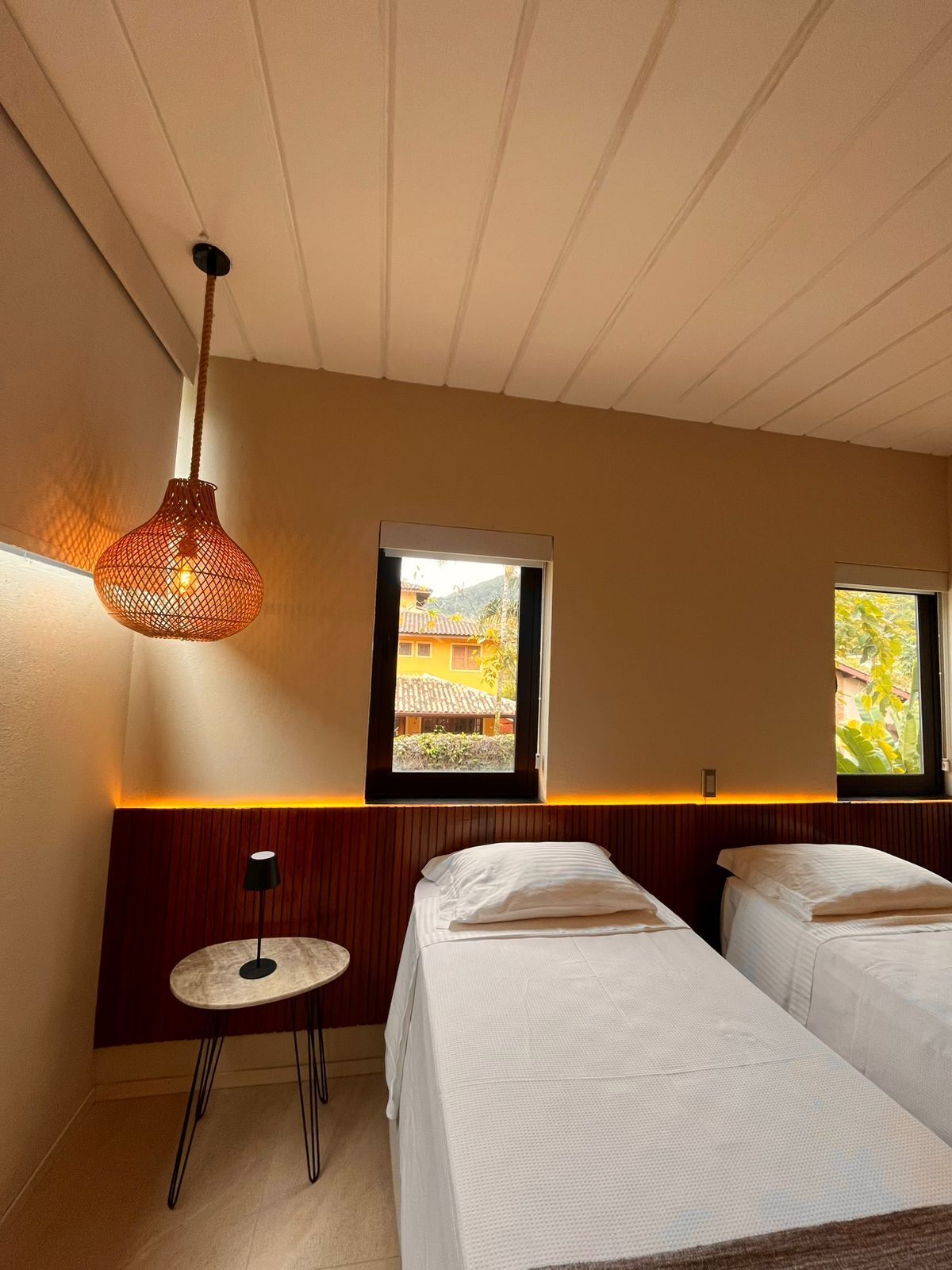 A room with two beds, a small round table, and a hanging light fixture.