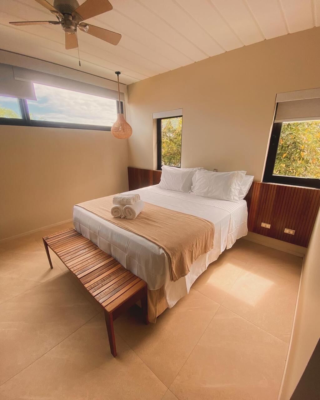 A bedroom with a bed, a bench, a ceiling fan, and windows.