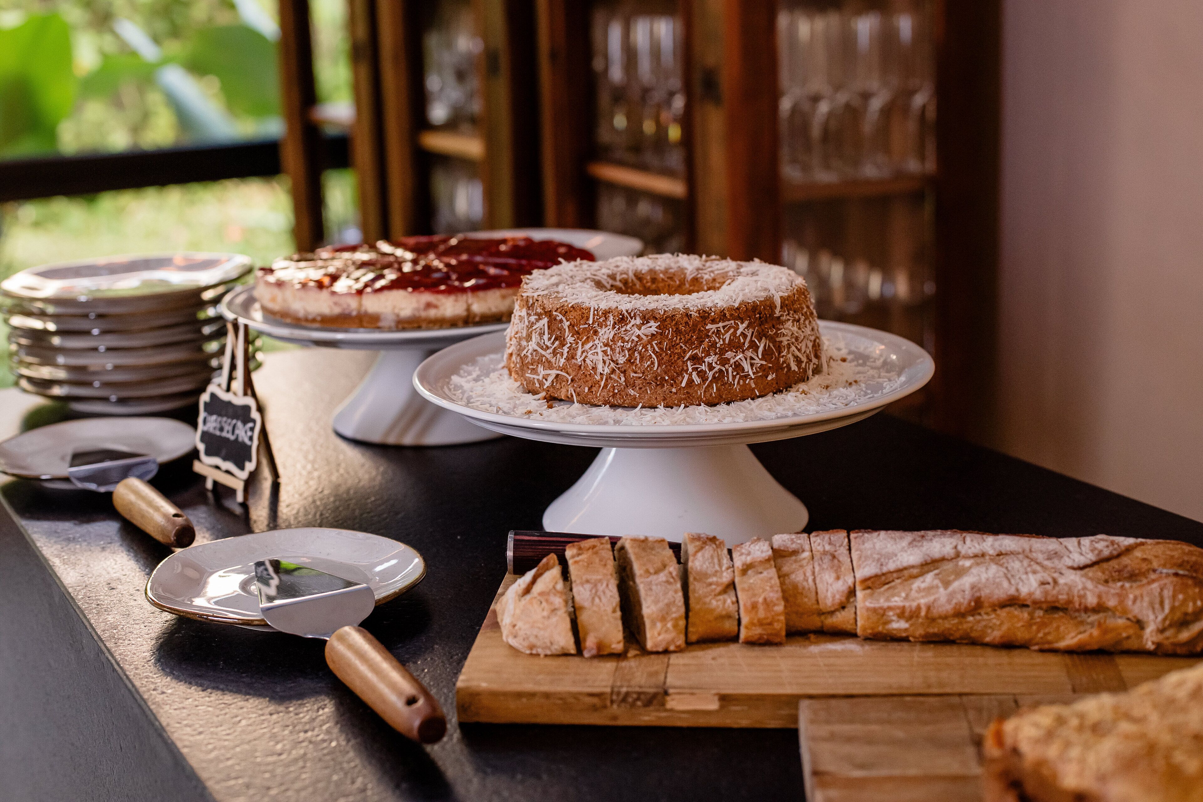A dessert display with cakes and a loaf of bread on a wooden board.