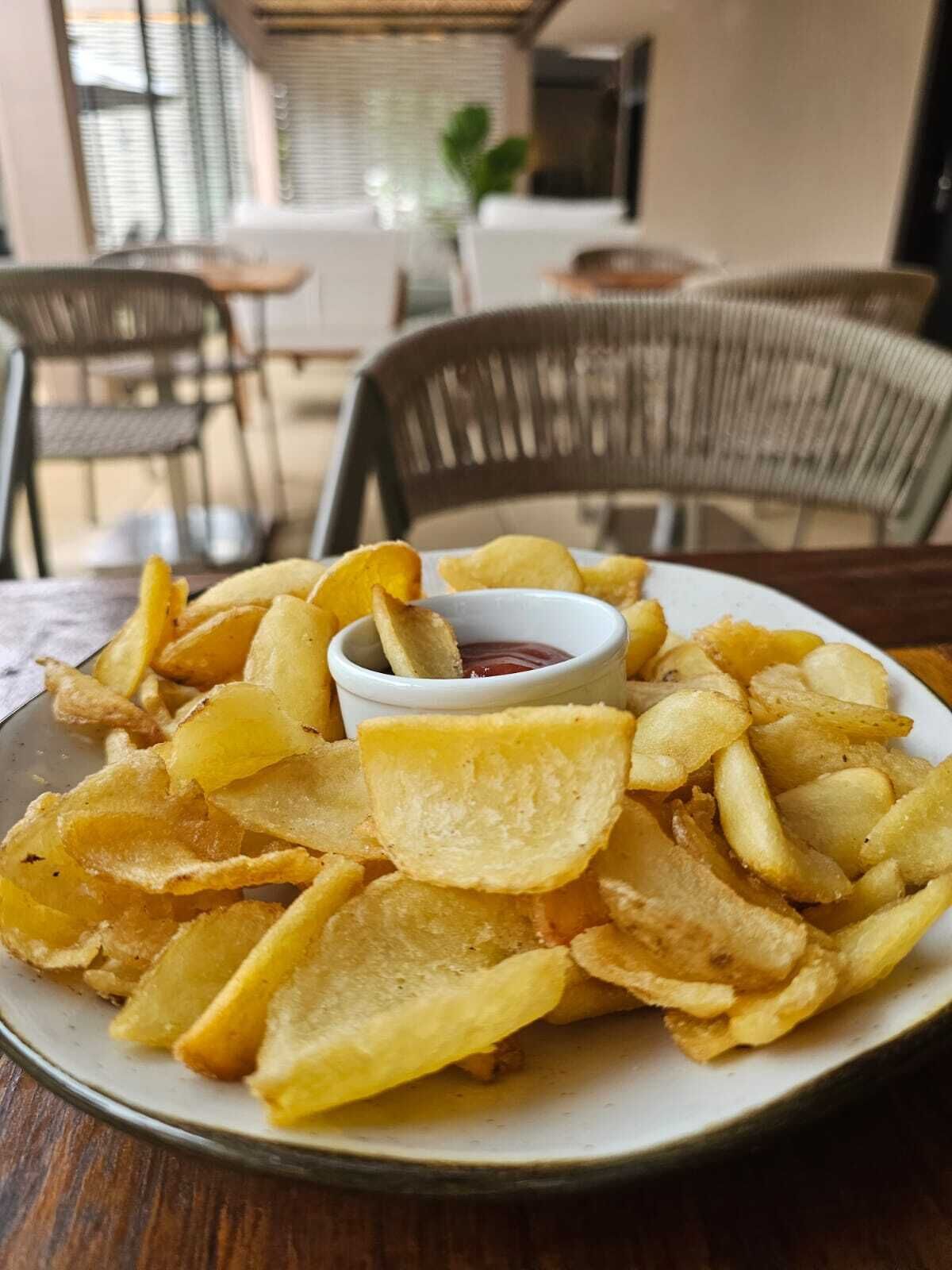 Un plato de deliciosas patatas fritas doradas con un recipiente pequeño de salsa roja.