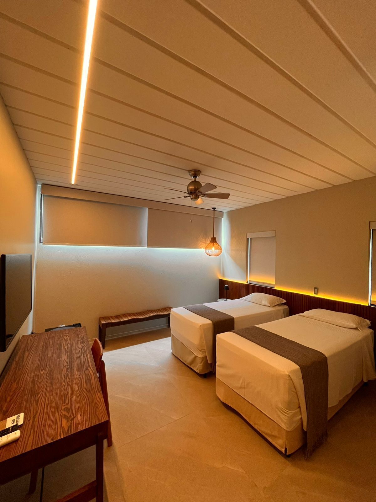 Una habitación de hotel con dos camas, una mesa de madera, un ventilador de techo y un televisor.