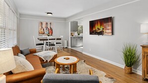 A modern living room with a sofa, coffee table, and artwork. There is a dining area with chairs and a table, and a kitchen in the background. - The Lockheed Lady - 3/2 Renovated Ranch in Marietta (Marietta)