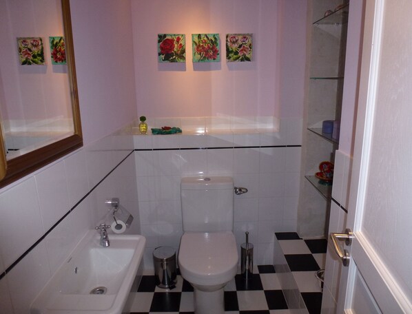 A bathroom with a sink, toilet, and a mirror. There are three paintings on the wall above the toilet.