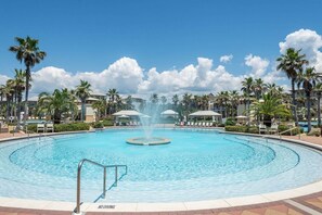 A large circular pool with a central fountain, surrounded by palm trees and lounge chairs. - GORGEOUS 4/4 SLEEPS 10! GULF VIEW FROM 3rd FLOOR! NEWLY FURNISHED!!! ONE BLOCK FROM BEACH ACCESS! (Panama City Beach)