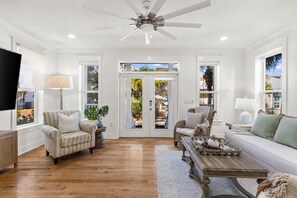 A spacious living room with a ceiling fan, wooden flooring, and a view through glass doors to an outdoor area. - GORGEOUS 4/4 SLEEPS 10! GULF VIEW FROM 3rd FLOOR! NEWLY FURNISHED!!! ONE BLOCK FROM BEACH ACCESS! (Panama City Beach)
