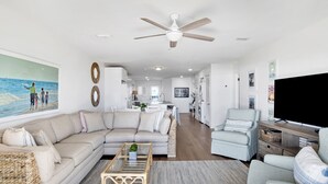 A modern living room with a beige sofa, a coffee table, a TV, and a ceiling fan. - Relaxing Beachfront Getaway | Gulf Shores Favorite (Gulf Shores)