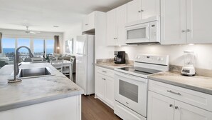 A modern kitchen with white cabinets, a built-in oven, a microwave, and a coffee maker. - Relaxing Beachfront Getaway | Gulf Shores Favorite (Gulf Shores)