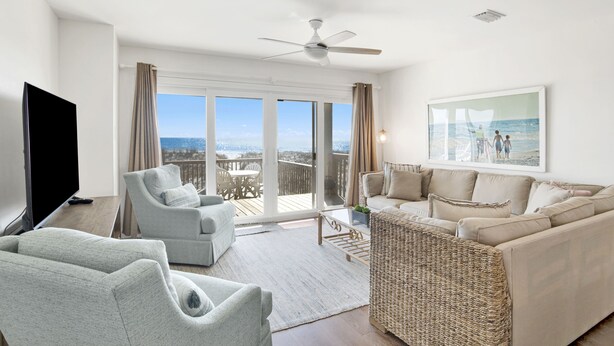 A spacious living room with a large sofa, a television, and a balcony with a view of the ocean. - Relaxing Beachfront Getaway | Gulf Shores Favorite (Gulf Shores)