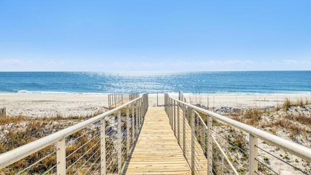Un muelle de madera que conduce a una playa bajo un cielo azul despejado.