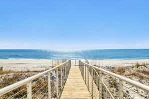 Un muelle de madera que conduce a una playa bajo un cielo azul despejado.
