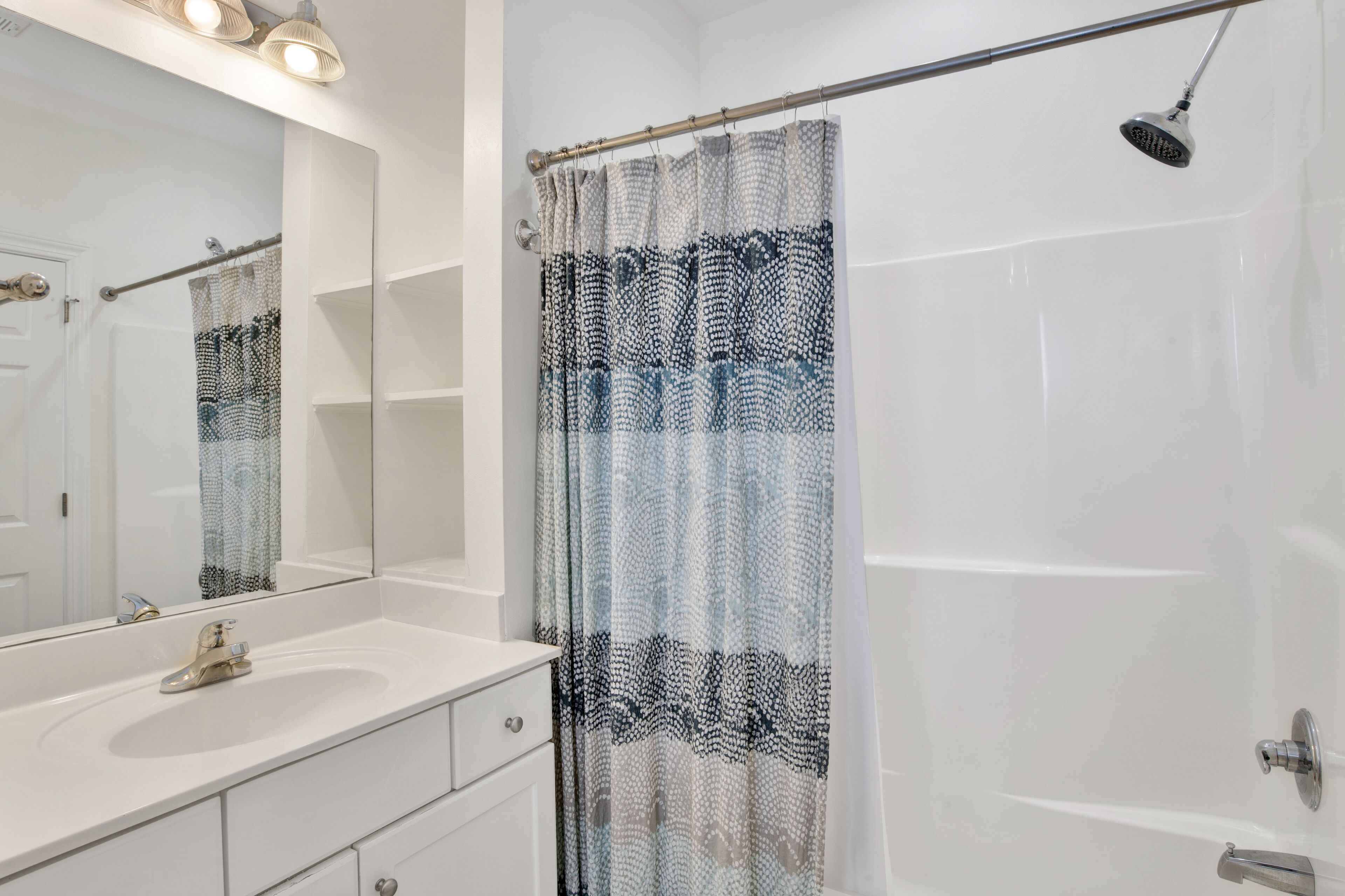 A bathroom with a white sink, a mirror, a shower with a patterned curtain, and a handheld showerhead.