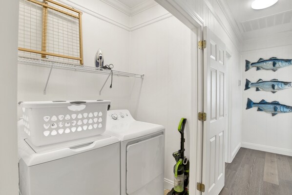 A laundry area with a washing machine, dryer, and iron. There are fish wall art and a door with a handle.