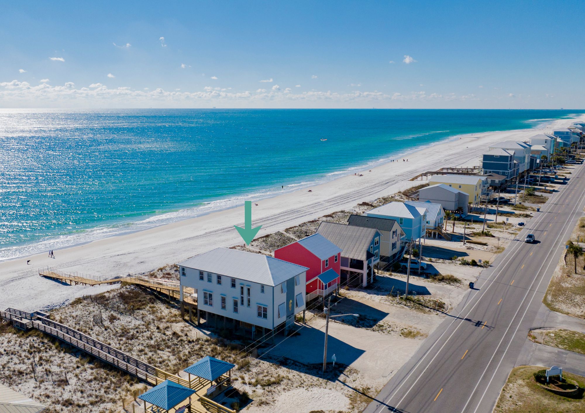 A coastal road with beachfront properties, a beach, and a clear sky.