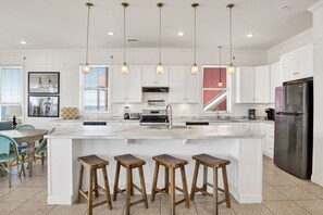 Una cocina moderna con una isla grande, luces colgantes y un refrigerador de acero inoxidable.