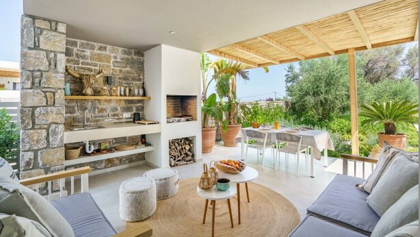 Un espacio exterior moderno con un muro de piedra, una chimenea y un porche cubierto.