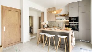 Una cocina moderna con una isla central, taburetes de bar, electrodomésticos integrados y una puerta de madera.