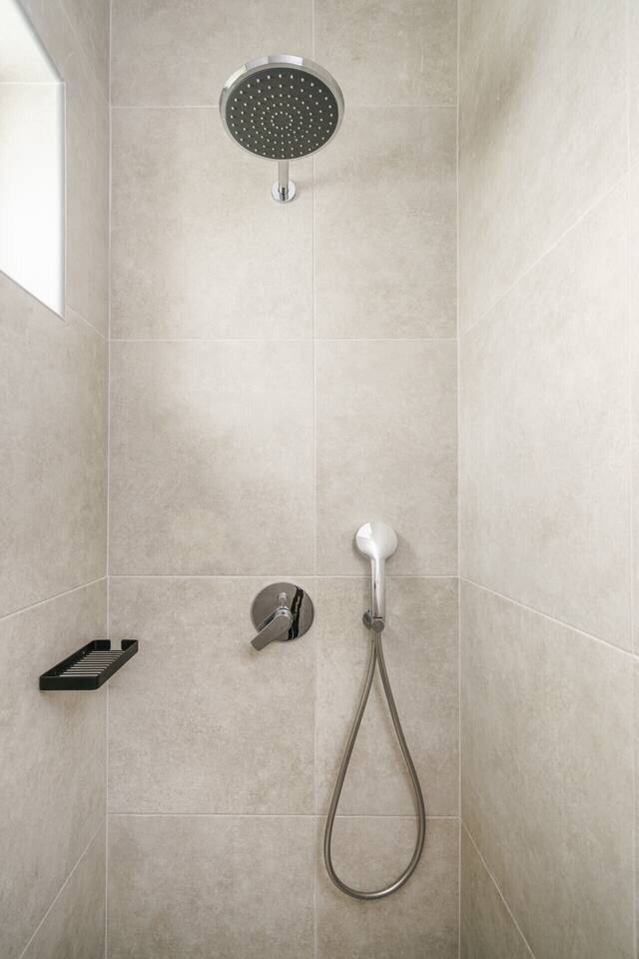 Een douche met een handdouche en een wanddouche in een betegelde badkamer.