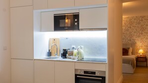 Una kitchenette compacta con un microondas Bosch, horno empotrado, pileta y tabla de cortar de madera.