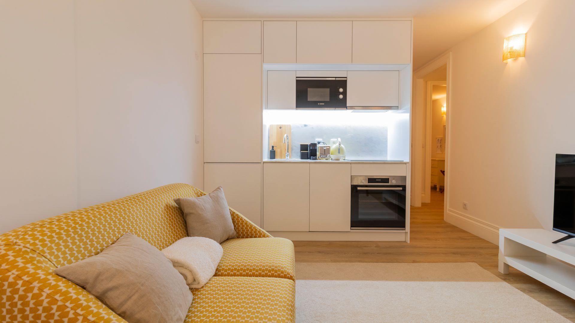 Un espacio habitable compacto con sofá, televisor, kitchenette y un pasillo.