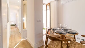 A modern dining area with a round table set for four, wicker chairs, and a view of the balcony through the open door. - Urban House Marquês - B - by LovelyStay (Porto)