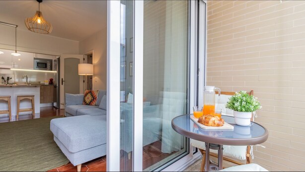 A modern living room with a sofa, a dining table with a plant and breakfast items, and a kitchen in the background. - Urban Retreat Porto by LovelyStay (Porto)