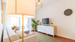 A modern living room with a sofa, a television on a wooden stand, a globe, and a clock on the wall. - Urban Retreat Porto by LovelyStay (Porto)