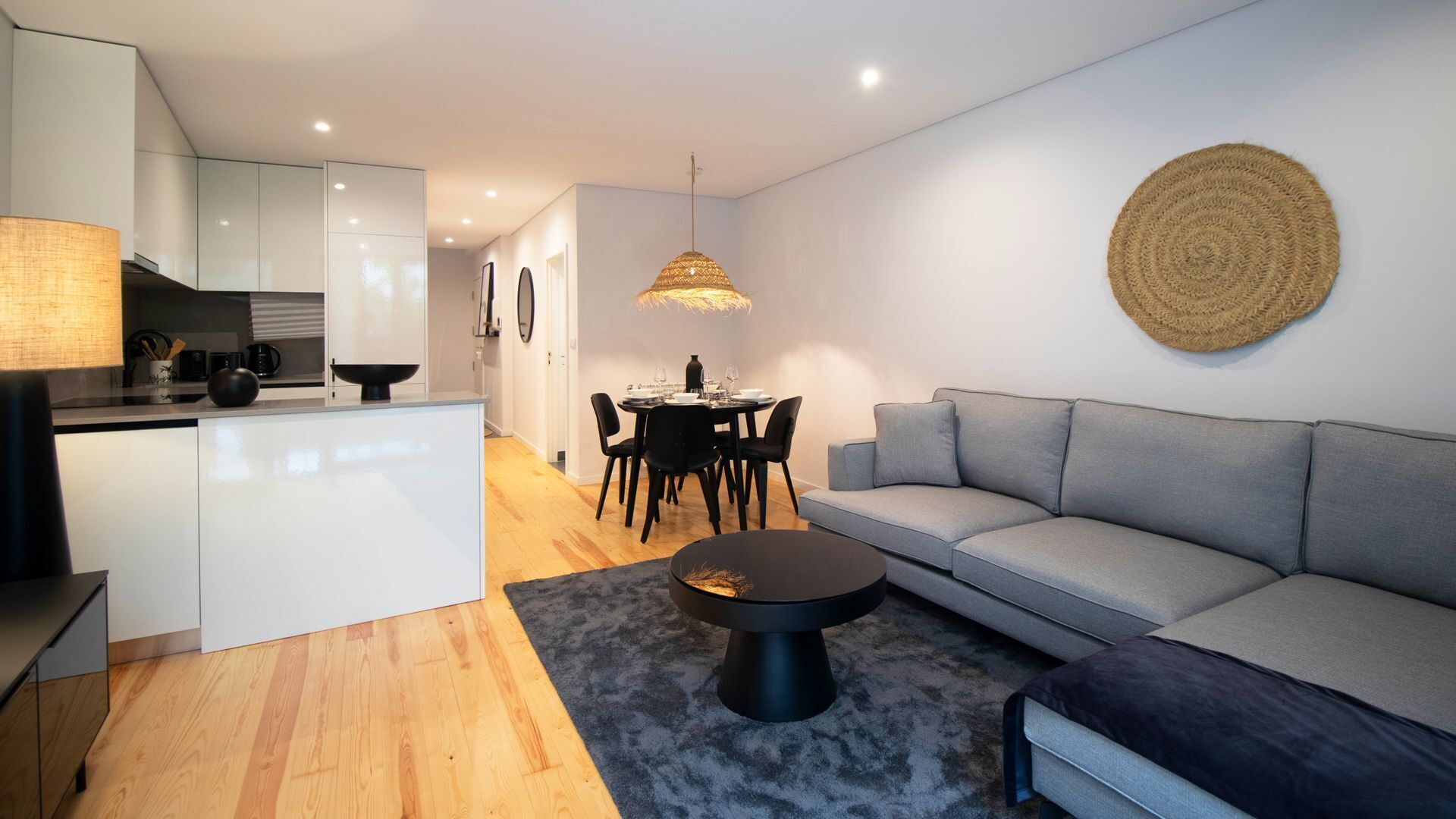A modern living room with a grey sofa, a round coffee table, and a dining area with a table and chairs.