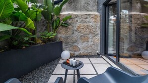 Un área de estar moderna al aire libre con un muro de piedra, plantas en macetas y una puerta de cristal que da a un patio.