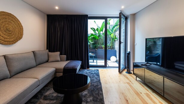 Una sala moderna con sofá, una mesa de centro, televisor y un ventanal corredero que da a un espacio exterior con plantas.