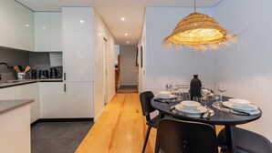 Una cocina moderna con armarios blancos, un comedor con una mesa redonda dispuesta para cuatro personas y una lámpara colgante de ratán.