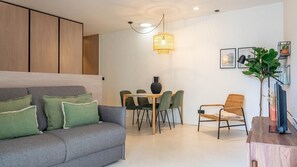 Un salon moderne avec un canapé gris, des coussins verts, une table à manger avec des chaises, un luminaire suspendu et une plante en pot.