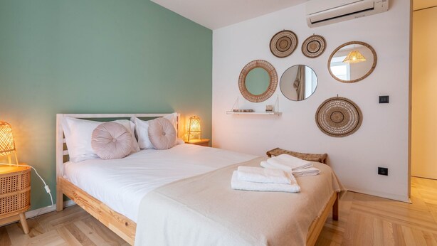 Un lit bien fait, avec du linge de lit blanc, une lampe de chevet et un climatiseur fixé au mur.