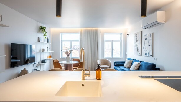 A modern kitchen with a central island, a dining area with chairs, a blue sofa, and artwork on the walls. - Penthouse w/ City Views | Almada 551 (Porto)