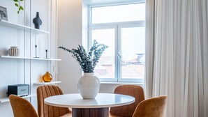 A modern dining area with a round table, two chairs, a vase with plants, and a bookshelf with decorative items. - Penthouse w/ City Views | Almada 551 (Porto)